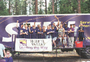 Workers and union organizers standing by a truck that says SEIU with the mountains in the background. The banner says Yosemittee Valley leading the way