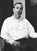 Josh Kirsch sitting in a chair, talking to the camera, he has on a white long sleve shirt
